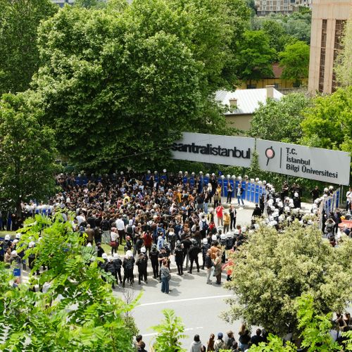 Free A large crowd gathers at the entrance of Istanbul Bilgi University surrounded by lush green trees. Stock Photo