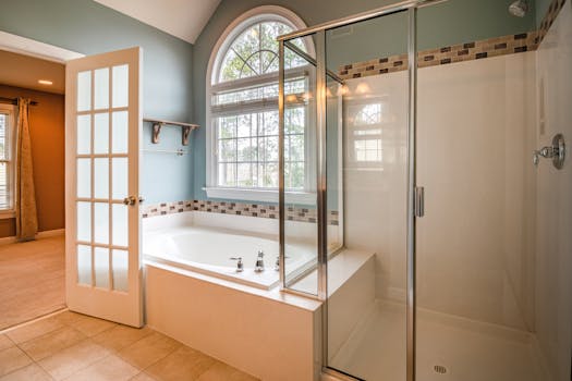 Spacious bathroom with elegant glass shower and white bathtub featuring arched window for natural light.