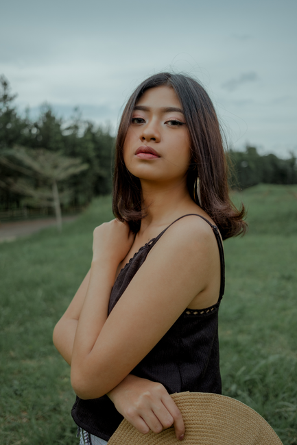 Elegant portrait of a young woman posing thoughtfully outdoors in a lush green setting.