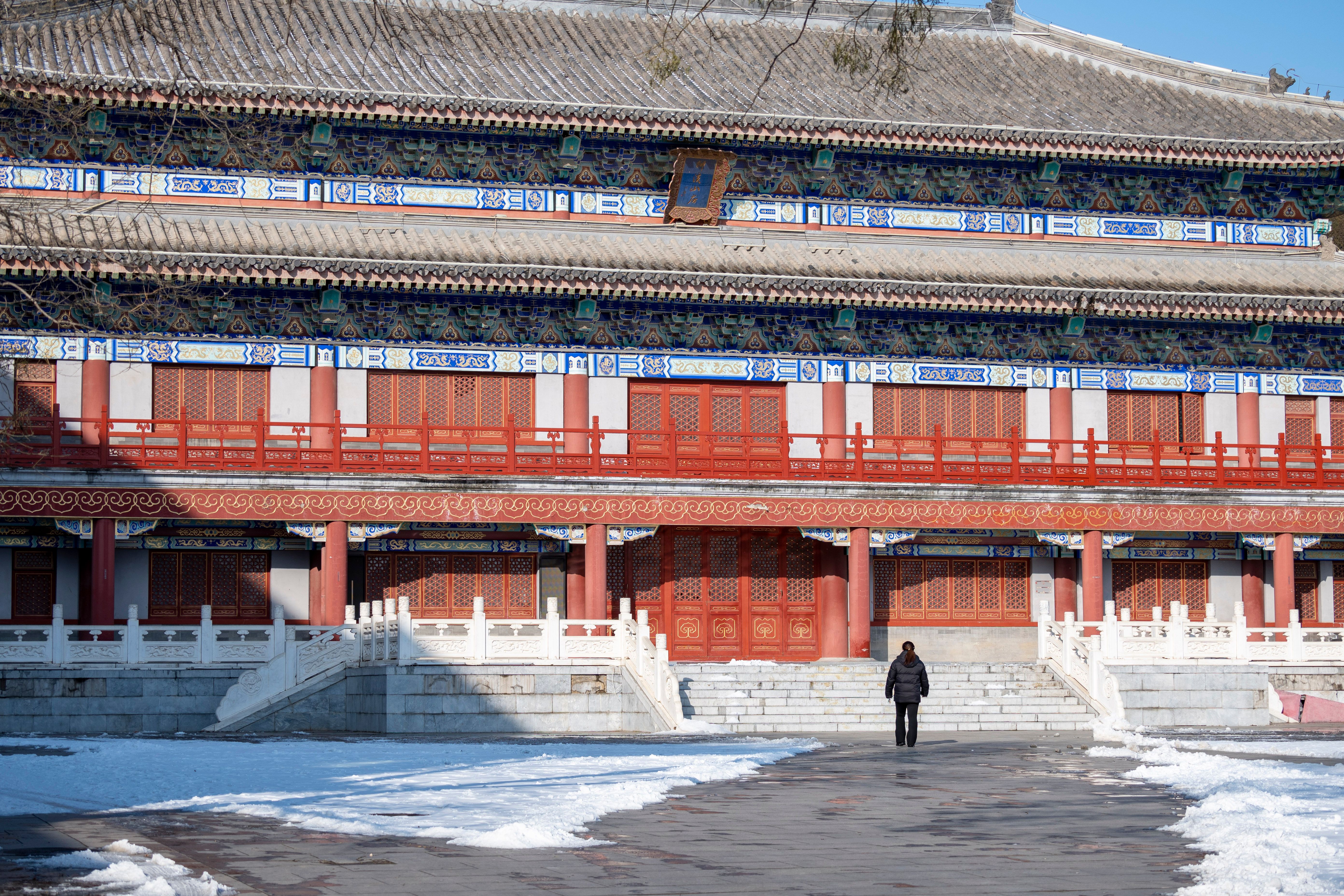 A person walks towards a traditional Chinese temple in snowy winter.