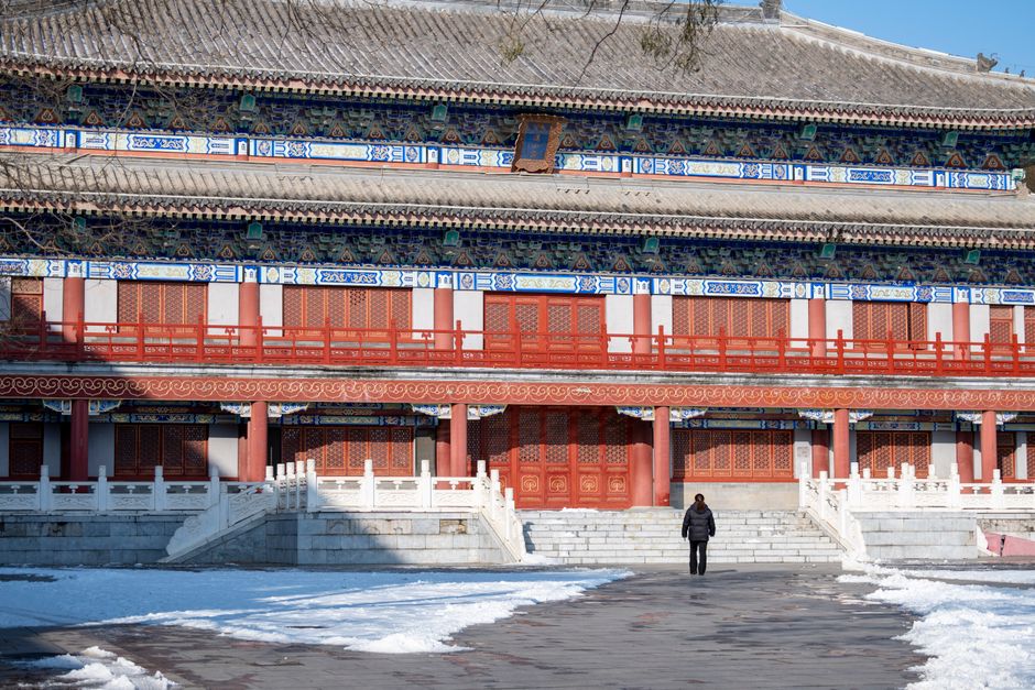 A person walks towards a traditional Chinese temple in snowy winter.