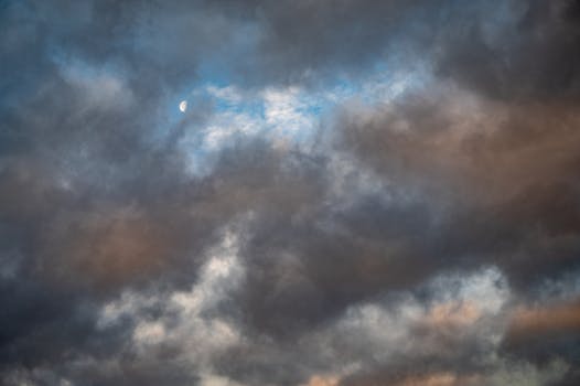 A dramatic sky filled with clouds revealing a glimpse of the moon. Perfect for weather themes.