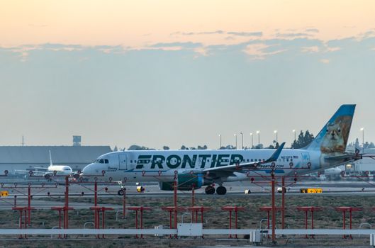 Frontier Airlines plane on runway at sunset, ready for departure.