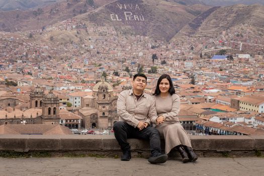 A couple poses in front of the scenic Cusco cityscape, with "Viva El Perú" visible on the hill.