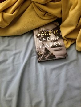 一个舒适的布置，展示了黛比·哈利在柔软床单上阅读《面对它》这本书