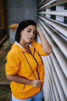 一位时尚女性身着黄色夹克，倚靠在户外的墙上