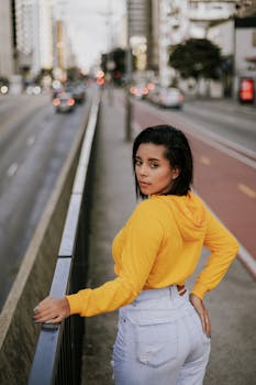 Stylish woman in yellow hoodie posing confidently on city street.