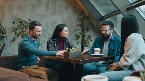 Free Four adults enjoy coffee and conversation in a modern cafe setting. Stock Photo