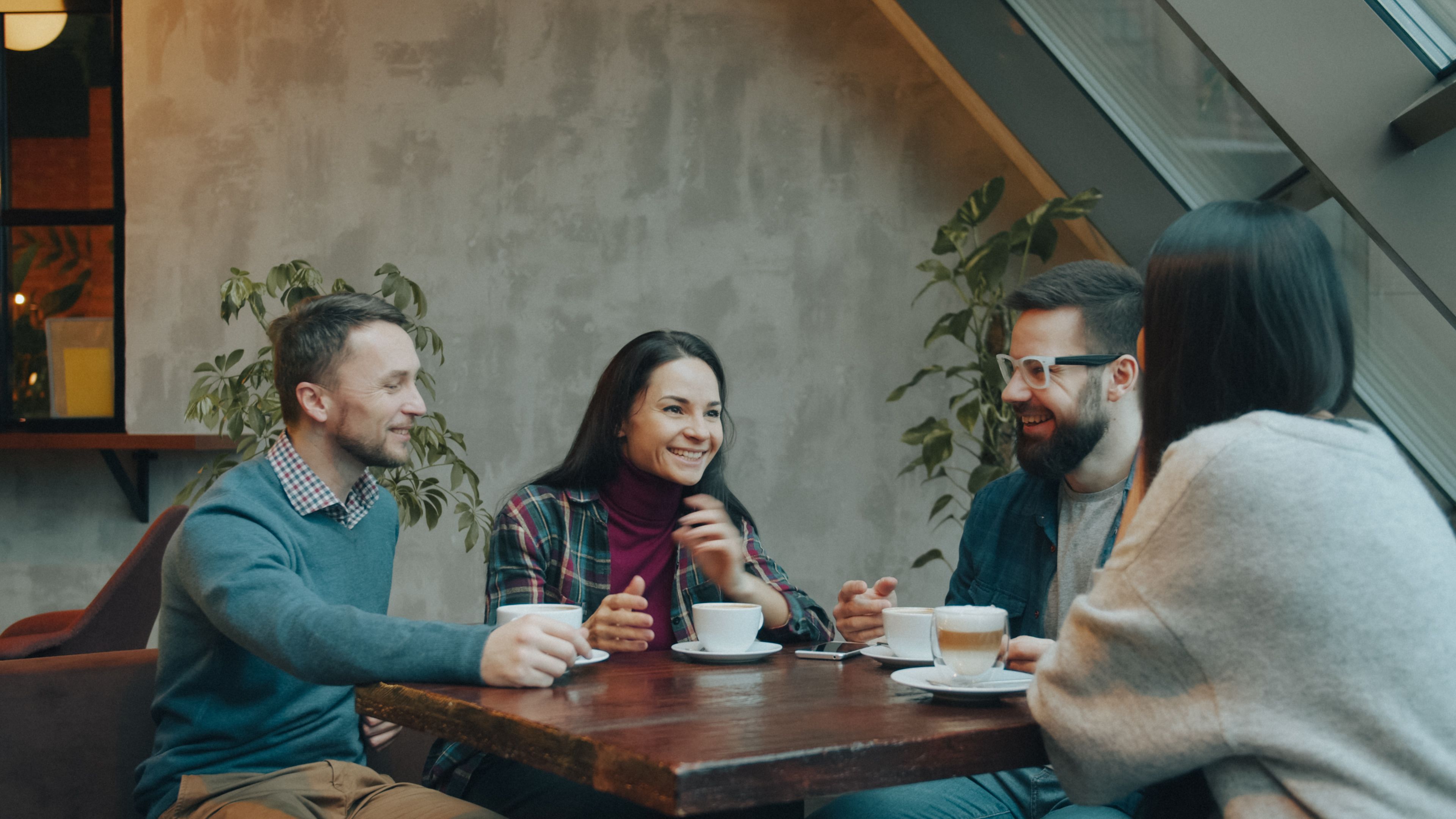 A group of friends laughing and drinking coffee in a modern, cozy cafe setting.