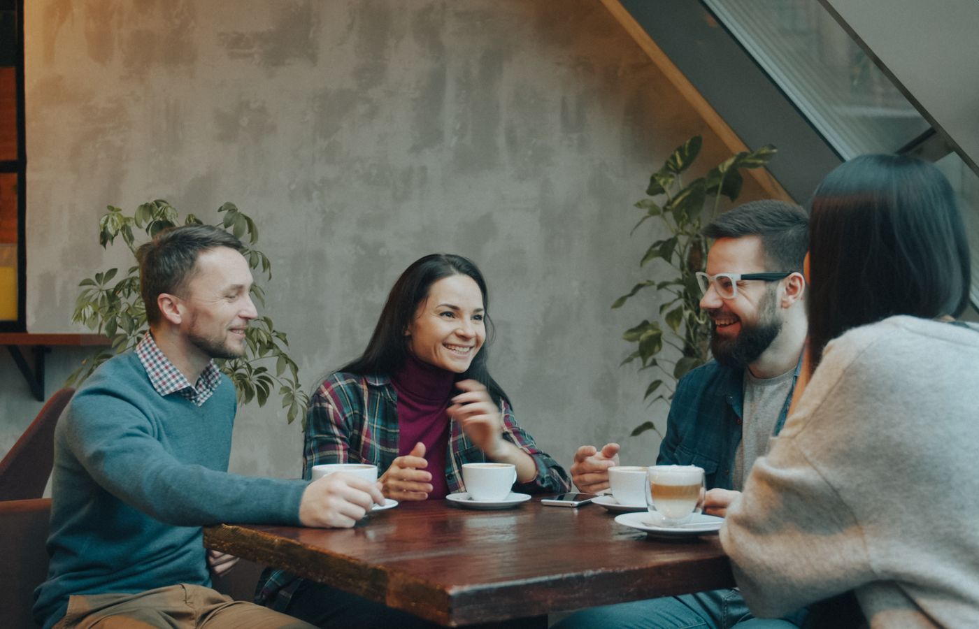 A group of friends laughing and drinking coffee in a modern, cozy cafe setting.