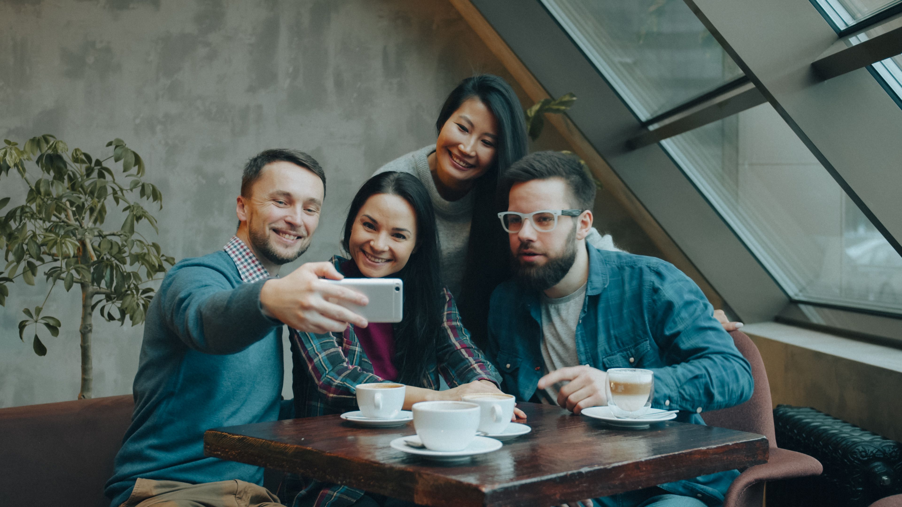 Four friends enjoy coffee and take a selfie in a cozy cafe setting.