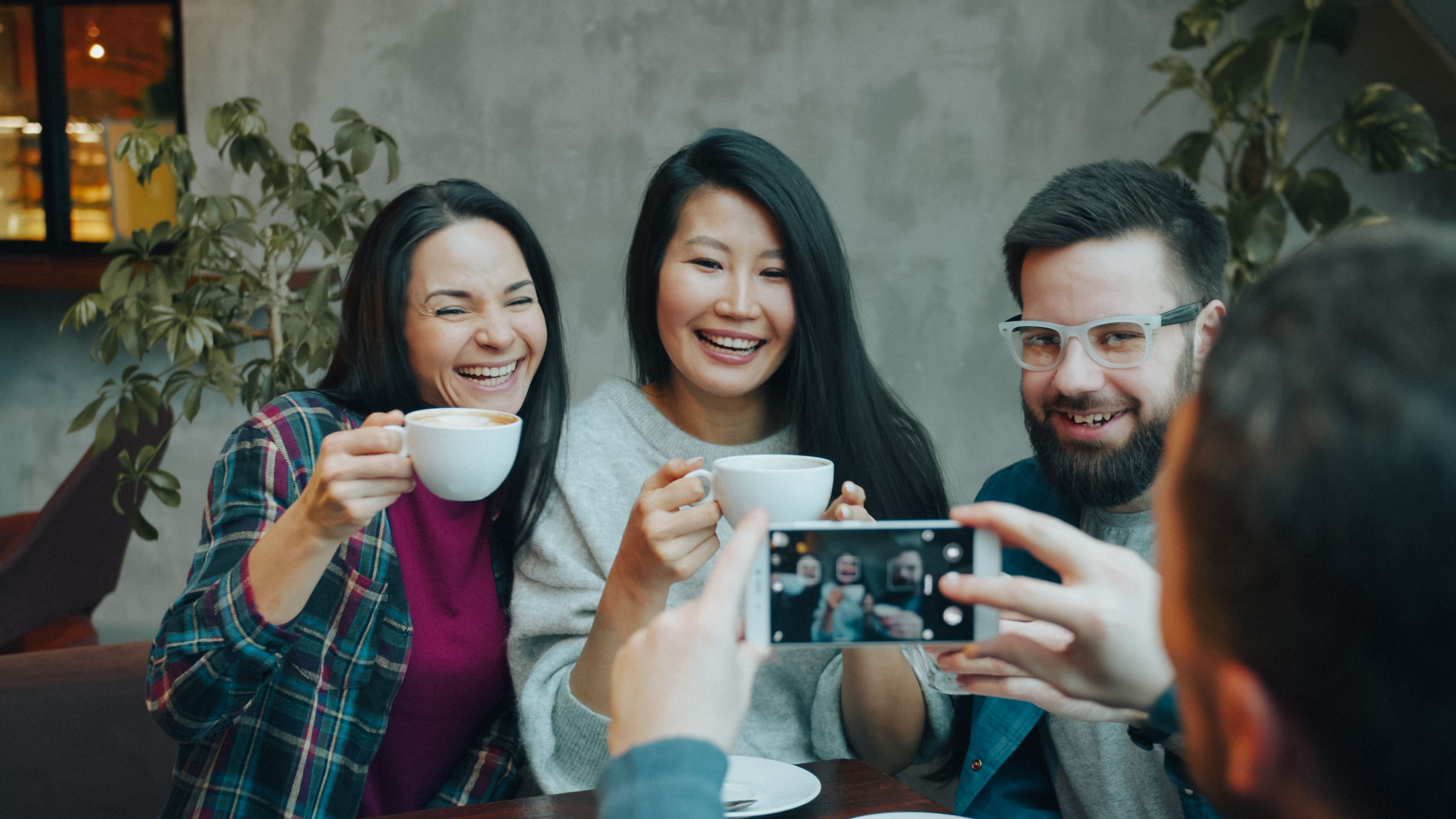 Three friends enjoy coffee and capture a selfie in a cozy cafe setting.