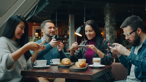 Free Friends capturing memories with their phones over coffee and croissants in a cozy cafe. Stock Photo