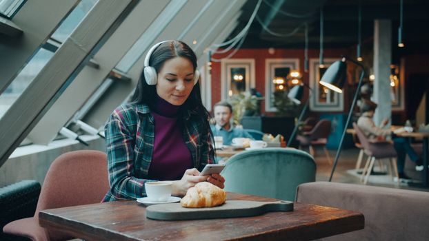Woman using phone and listening to music while sitting in a modern cafe.