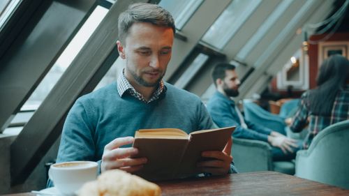 Free Adult man reading in a chic cafe, enjoying coffee and a croissant. Stock Photo