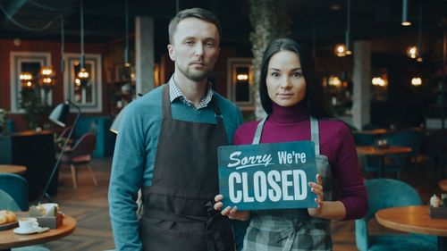 Free Two café owners holding a 'Sorry We're Closed' sign inside their restaurant. Stock Photo