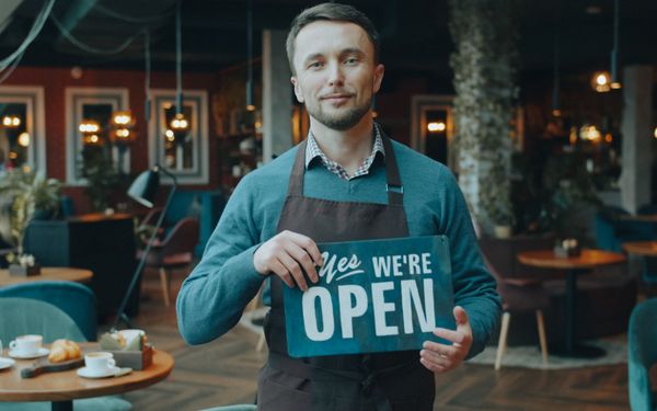 Cafe owner holding a sign that says we are open
