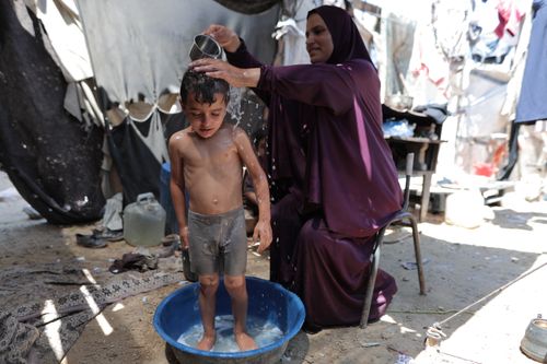Free A mother pours water on her child in a refugee camp, highlighting daily life challenges. Stock Photo