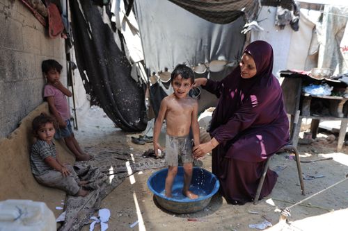 Free A mother bathes her child in an outdoor setting in Gaza Strip, surrounded by other children. Stock Photo