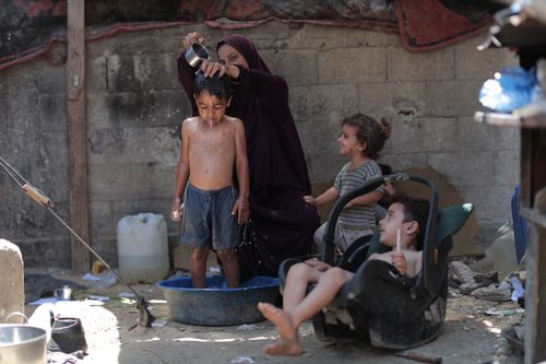 Free A mother bathes her child outdoors in Gaza, capturing everyday family life. Stock Photo