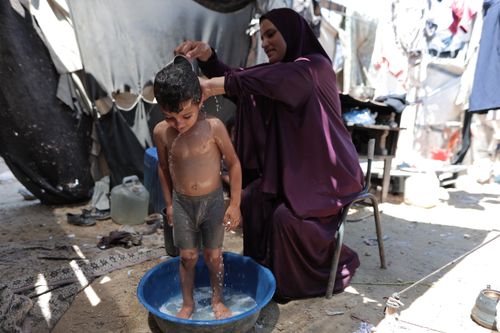 Free A mother washes her child in a makeshift tub outdoors, showcasing daily life in a refugee camp. Stock Photo