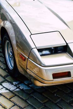 Detailed close-up of the headlight and bumper of a vintage car showcasing classic design features on a cobblestone surface.