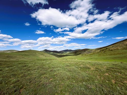 Free Vast green plateau with rolling hills and dramatic clouds on a clear summer day. Stock Photo