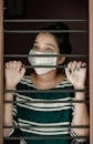 Woman in Green and White Stripe Shirt Covering Her Face With White Mask