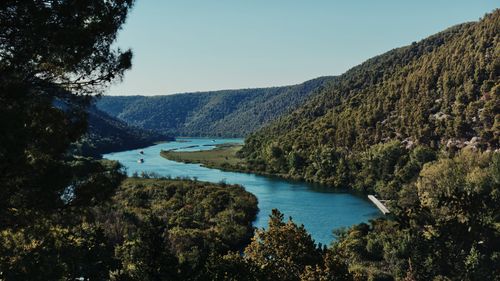 Free Aerial view of a meandering river flowing through a lush, green valley under a clear blue sky. Stock Photo