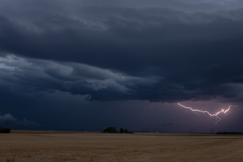 Free A striking image of a lightning storm illuminating the rural fields under a dark evening sky. Stock Photo