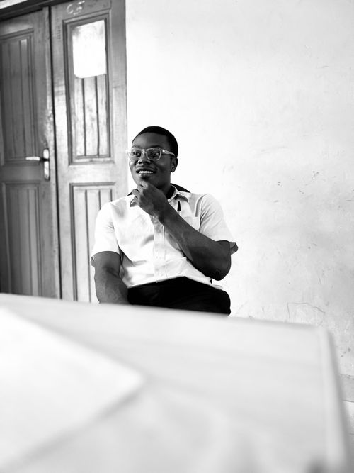 Free Black and white photo of a young man seated in a classroom, contemplating. Stock Photo