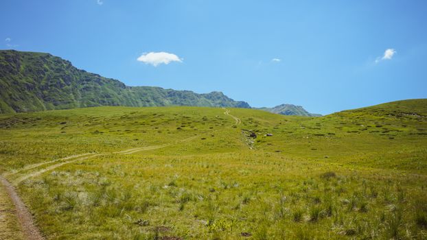 A peaceful grassy mountain landscape under a clear blue sky in Dibër County, Albania.