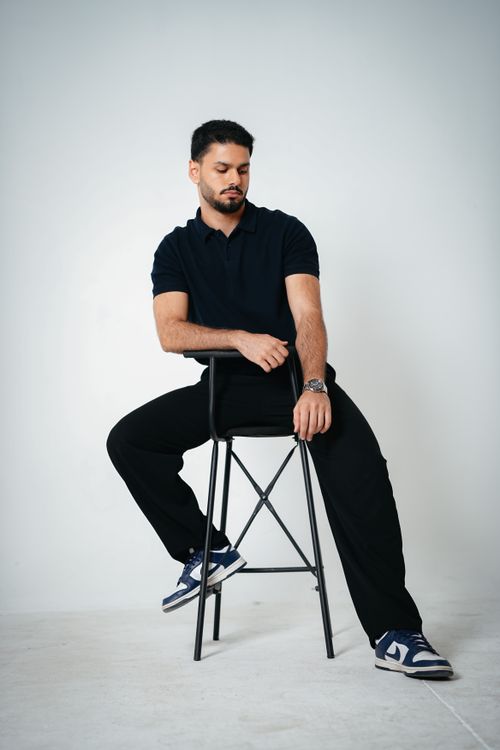 Free Portrait of a stylish male model seated on a stool in a minimalist studio setting, embodying confidence. Stock Photo