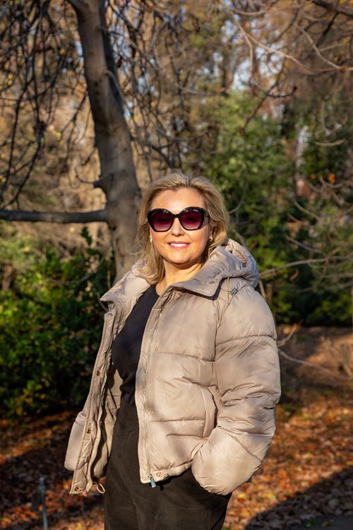 Free Smiling woman in sunglasses and winter coat enjoying a sunny day in a serene park setting. Stock Photo