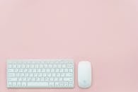 在柔和的粉红色背景上，白色键盘和鼠标显得干净而极简，非常适合女性办公室主题