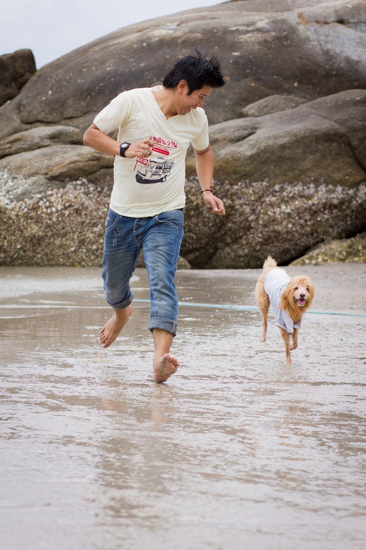 Man And His Pet Dog Running On The Shore