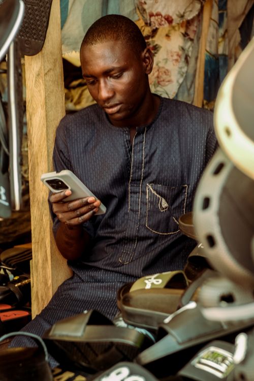 Free Man in traditional dress focused on smartphone among merchandise. Stock Photo