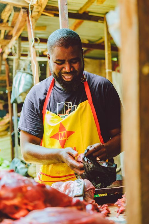 Free A cheerful butcher preparing meat at an outdoor market stall, wearing a bright apron. Stock Photo