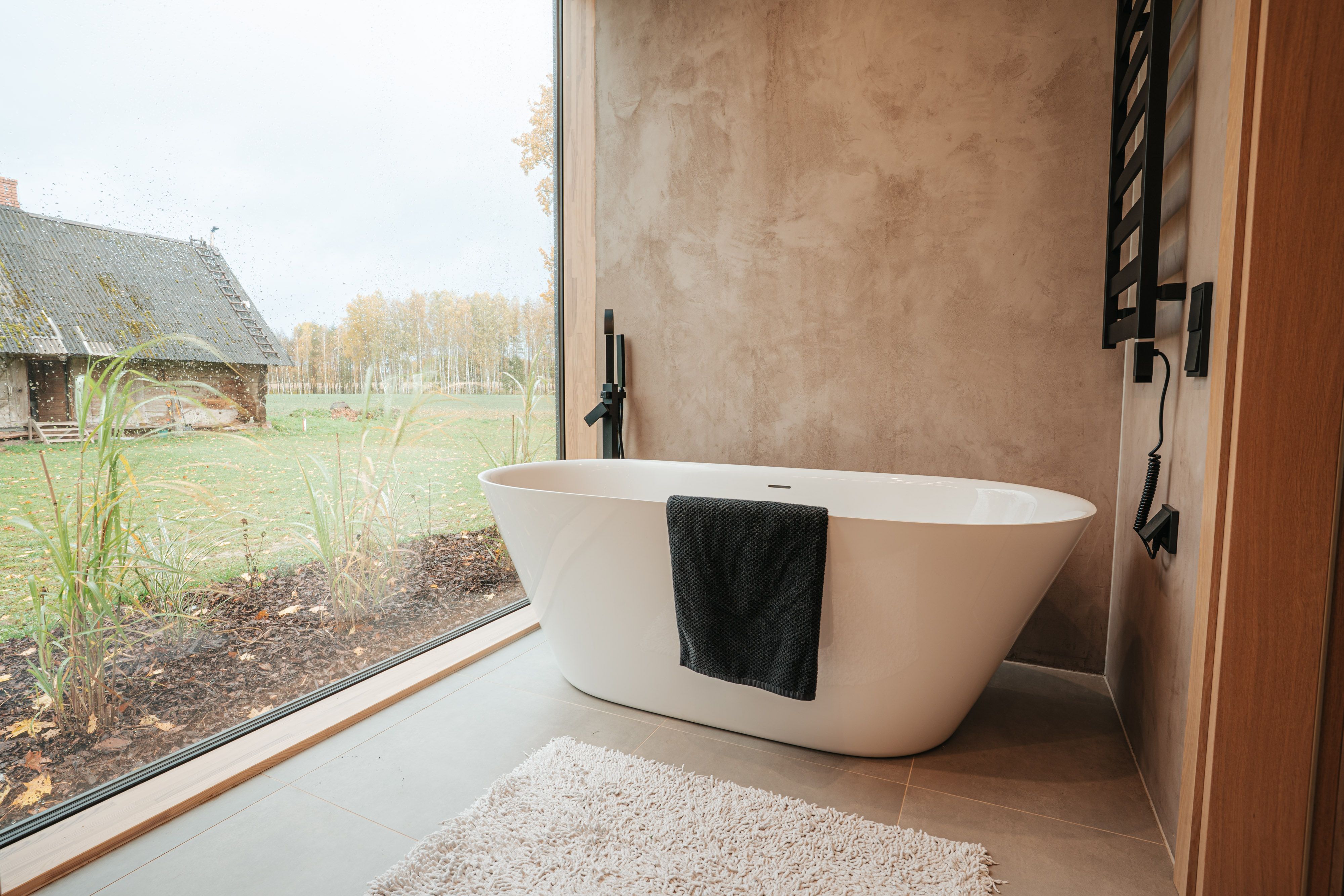 Modern bathtub in rustic bathroom overlooking serene countryside landscape.