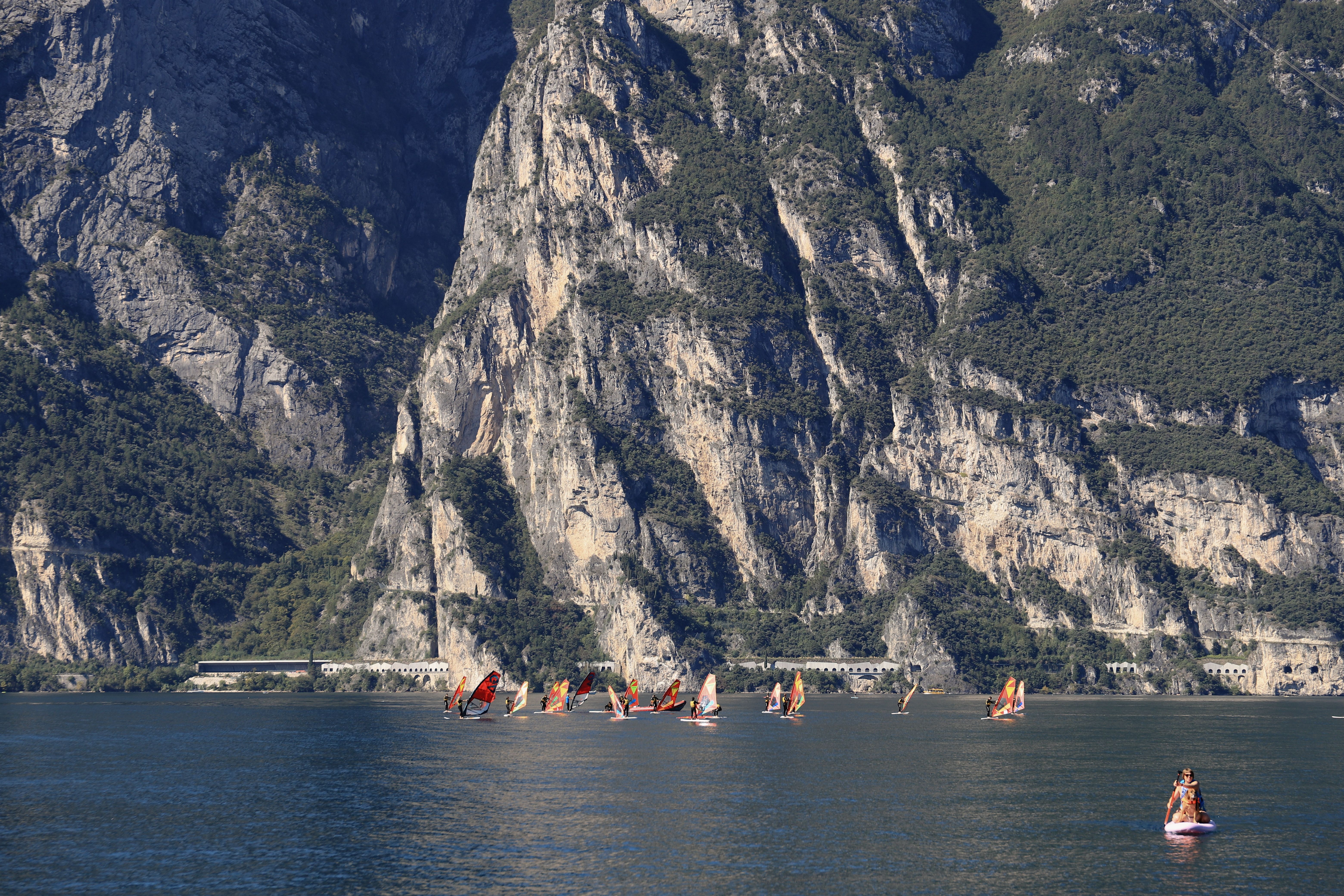 Windsurfers enjoying a sunny day on Lake Garda with the stunning backdrop of Italian mountains.