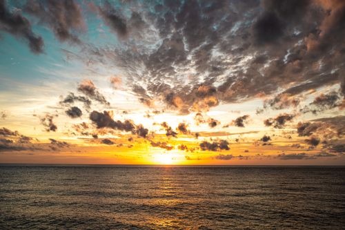 Free A breathtaking ocean sunset with vibrant colors and dramatic clouds reflecting on the water. Stock Photo