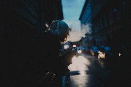 Woman in Black Jacket Standing on Sidewalk Smoking