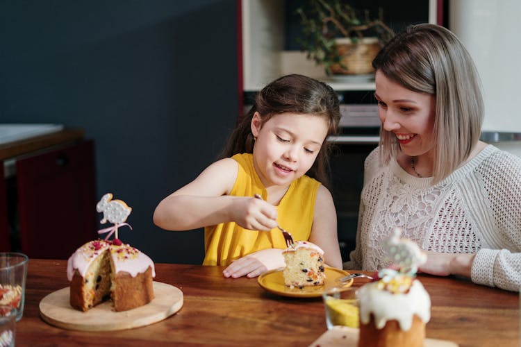 Mom And Daughter Eating Cake On Brown Wooden Table