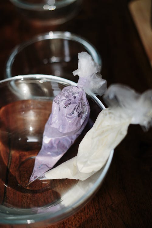 Clear Bowl with Water and White and Purple Icing Bag on Brown Wooden Table