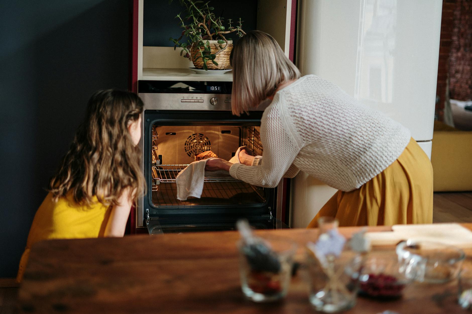 Mulher pegando alimento no forno junto com uma criança. Fazer sua própria comida ajuda a ter uma alimentação saudável!