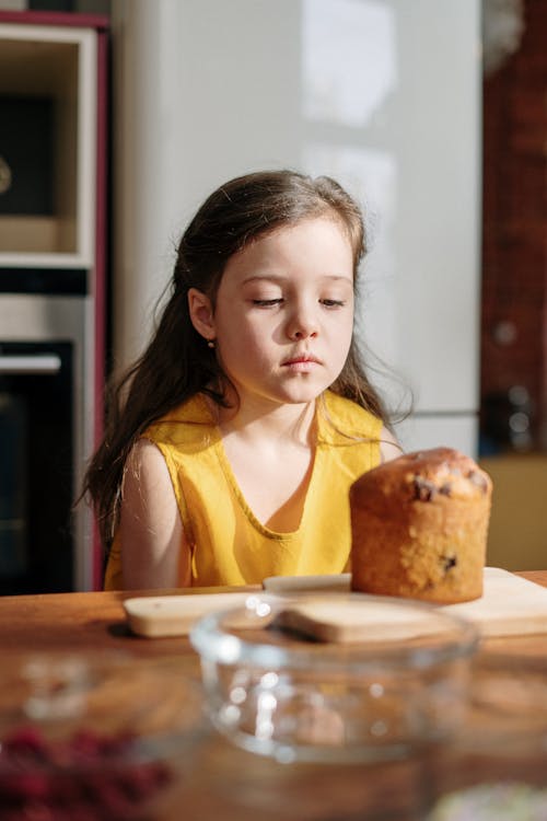 Girl in Yellow Shirt Sitting by the Table With Bread on Plate