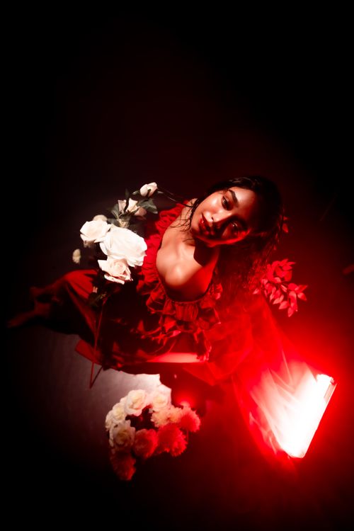 Free Artistic portrait of a woman in red light holding white roses, exuding a moody and dramatic vibe. Stock Photo