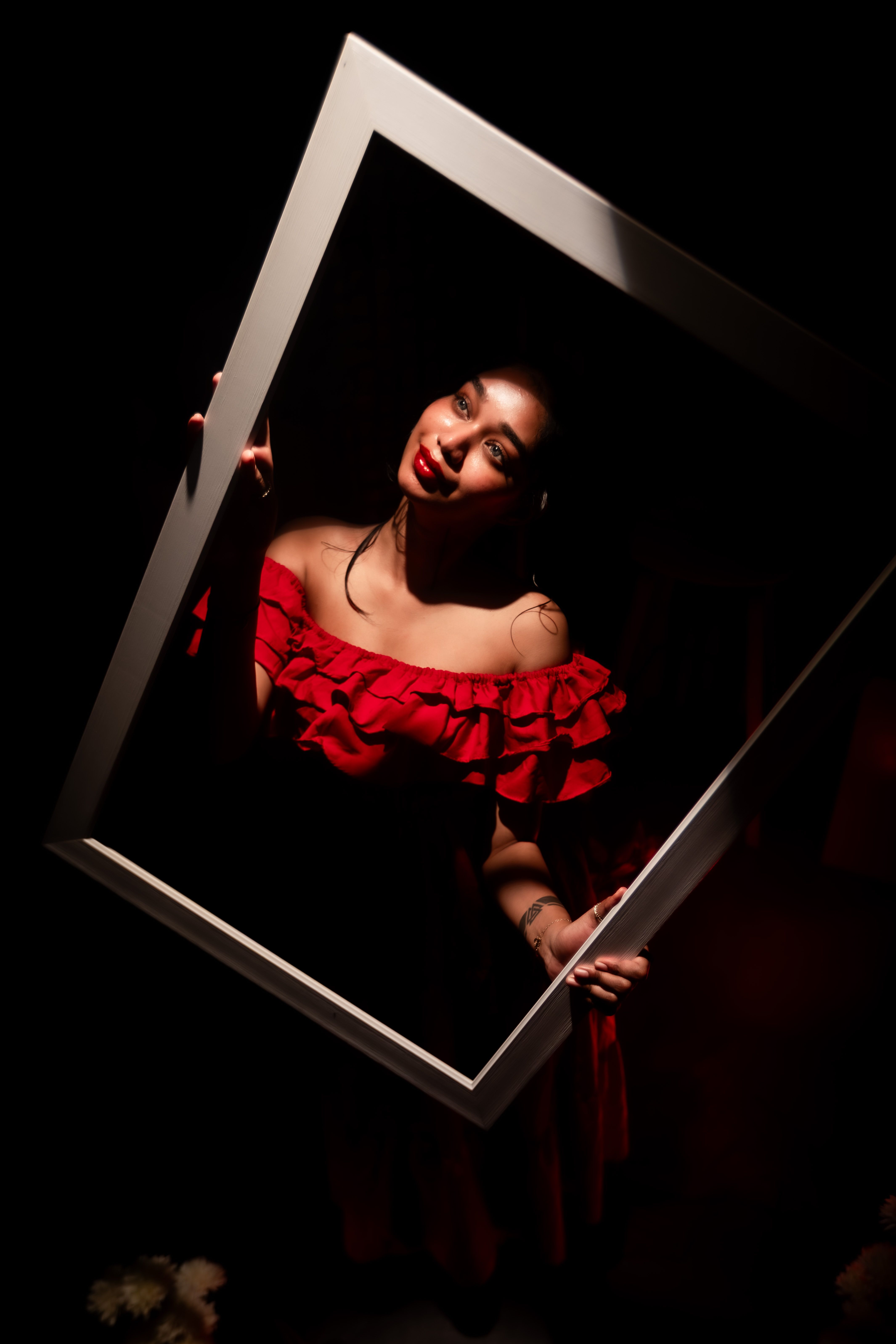 Artistic portrait of a woman in a red dress holding an empty frame against a dark background.