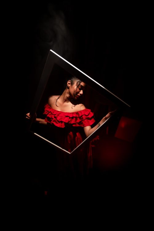 Free Dramatic portrait of a woman in a red dress holding a frame against a dark background. Stock Photo