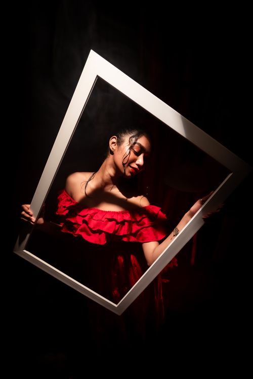 Free Dramatic lighting on woman in red dress holding frame, creating artistic portrait. Stock Photo